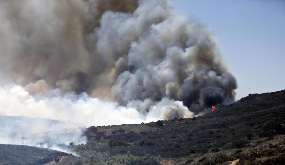 Billowing smoke rises from flames as firefighters begin the trek up the hills to battle a wild fire, Tuesday, May 13, 2014, in San Diego. Wildfires destroyed a home and forced the evacuation of several others Tuesday in California as a high-pressure system brought unseasonable heat and gusty winds to a parched state that should be in the middle of its rainy season. (AP Photo)