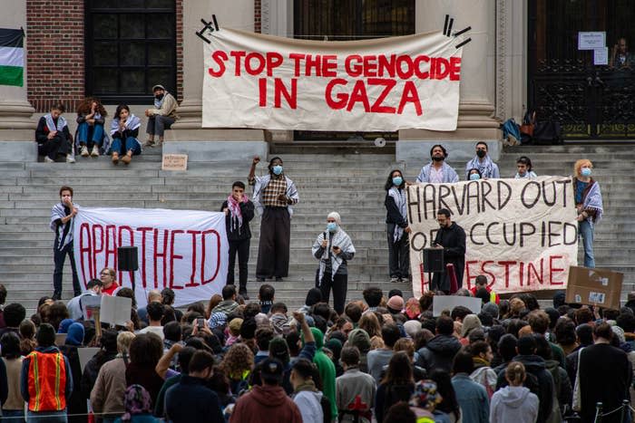 Protesters with banners advocating against conflict in Gaza and banner saying "STOP THE GENOCIDE IN GAZA" in background