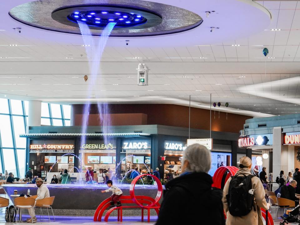 Inside an airport terminal with a man on the left walking toward a restaurant stand behind a fountain