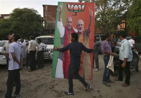 An activist of India's main opposition Bharatiya Janata Party (BJP) carries a hoarding featuring India's Hindu nationalist Narendra Modi (R) and Rajnath Singh, president of the BJP, during celebrations before Modi was crowned as the prime ministerial candidate for the party, in Jammu September 13, 2013. REUTERS/Mukesh Gupta