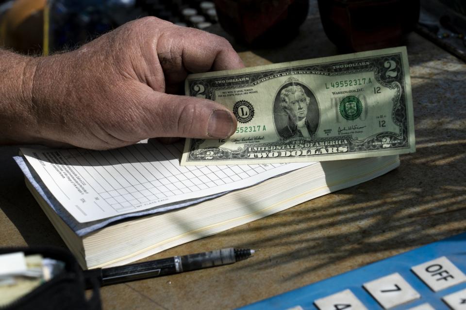 A hand resting on a receipt book holds a $2 bill