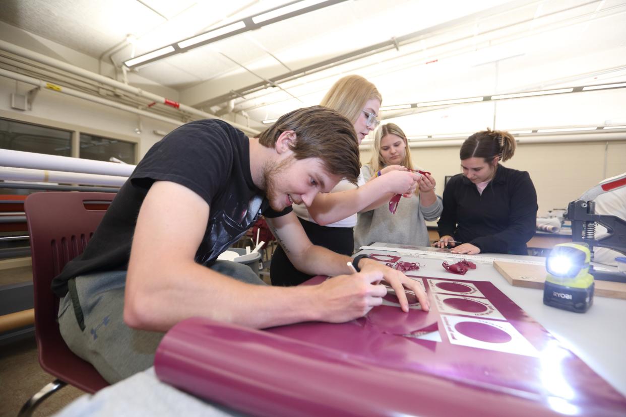 Canal Winchester High School senior Zade Fusselman (left), senior Emily Williamson, junior Elayna Griffith and senior Montana Steward, remove excess from a piece out of a vinyl printer May 5 during a work-based learning class in the Canal Creations print production lab at the school.