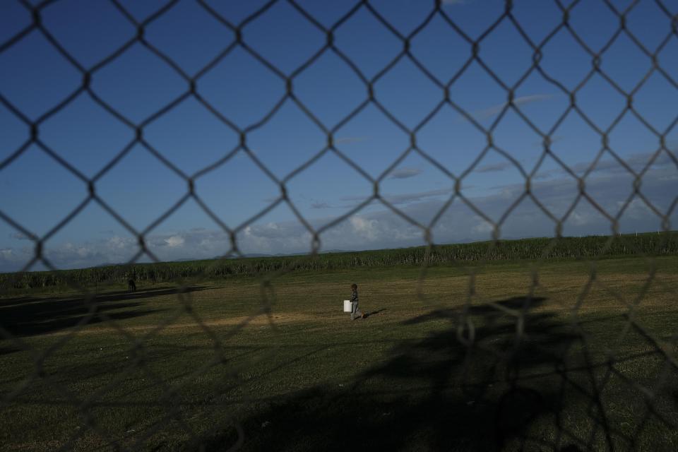 A Haitian child carries a container filled with water across an improvised soccer field in the Batey La Lima community, in La Romana, Dominican Republic, Wednesday, Nov. 17, 2021. Human rights activists are accusing the Luis Abinader government of targeting Haitian migrants, separating children from their parents and racial profiling. (AP Photo/Matias Delacroix)