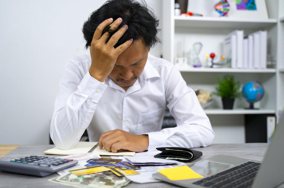 A man with his head in his hands in front of a pile of bills and a calculator.