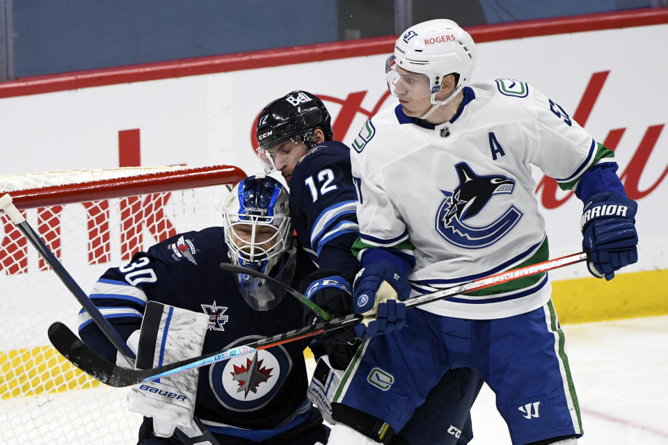 Vancouver Canucks' Tyler Myers (57) checks Winnipeg Jets' Jansen Harkins (12) into Jets goaltender Laurent Brossoit (30) during second-period NHL hockey game action in Winnipeg, Manitoba, Monday, May 10, 2021. (Fred Greenslade/The Canadian Press via AP)