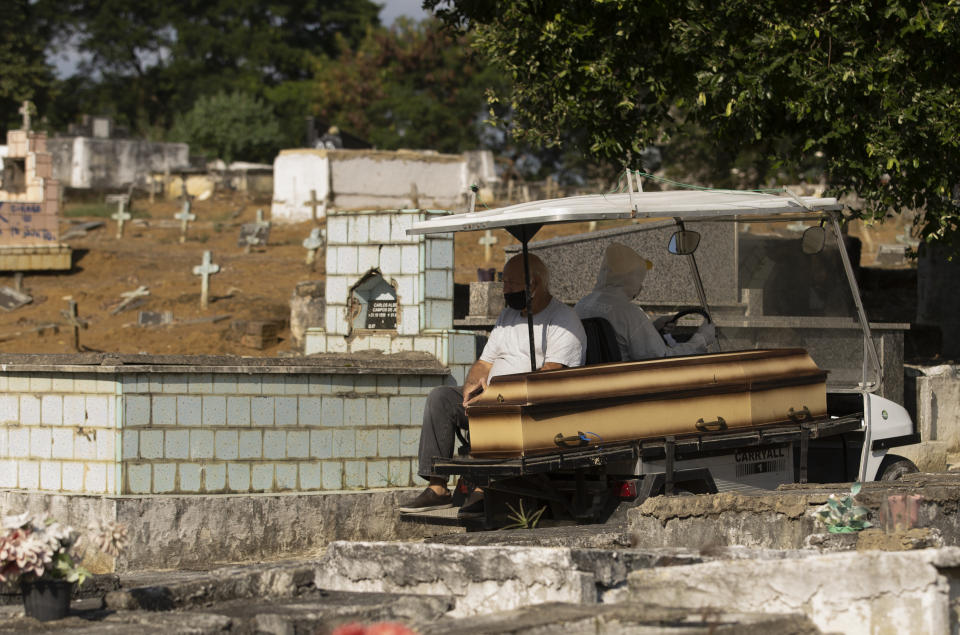 A man wearing a mask sits next the coffin of his mother as he's transported by a cemetery worker in a full protection suit to her burial site at the Nossa Senhora das Gracas cemetery in Duque de Caxias, Rio de Janeiro, Brazil, Monday, April 27, 2020. The woman's body was previously being held in a refrigerator for confirmed and suspected victims of of COVID-19, according to the administration of the cemetery. (AP Photo/Silvia Izquierdo)