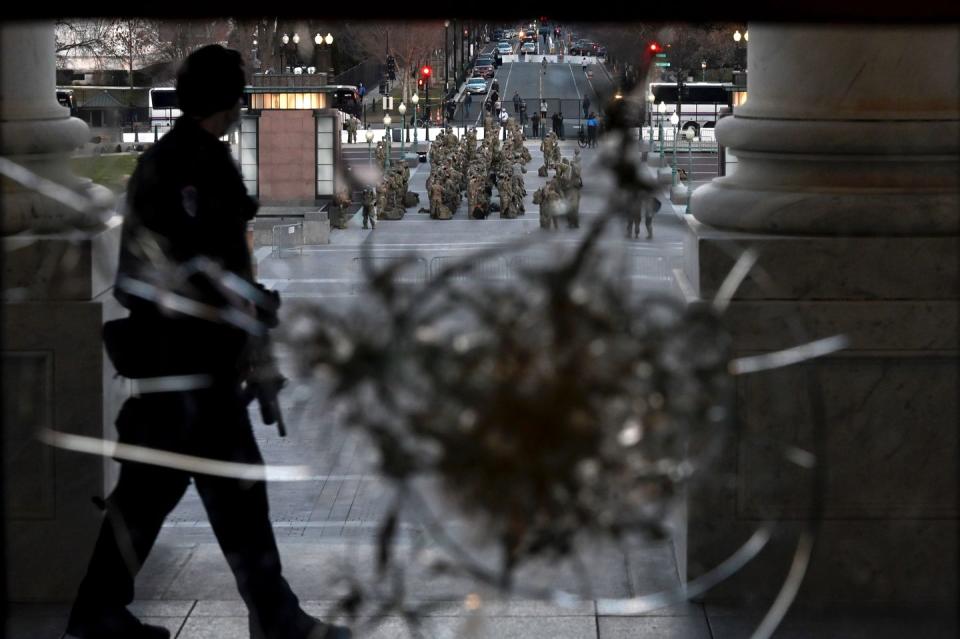 <p>A member of the Capitol police walks past a damaged door as members of the US National Guard stand at attention outside at Capitol Hill in Washington, DC on January 12, 2021.</p>