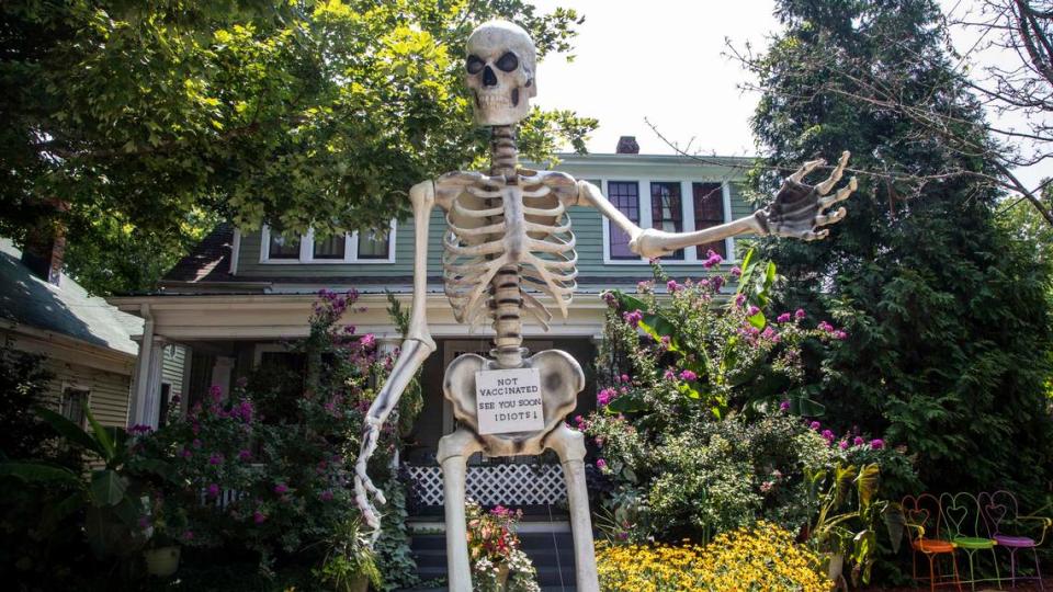 A 13-foot skeleton telling people to vaccinate or die and mock tombstones are on display at the home of Jesse Jones in Raleigh’s Oakwood neighborhood.