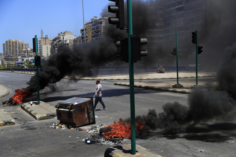 FILE - In this Thursday, June 17, 2021 file photo, a protester passes burning tires and garbage containers blocking a main highway during a protest against the increase in prices of consumer goods and the free fall of the local currency, in Beirut, Lebanon. Lebanon is struggling amid a 20-month-old economic and financial crisis that has led to shortages of fuel and basic goods like baby formula, medicine and spare parts. The crisis is rooted in decades of corruption and mismanagement by a post-civil war political class. (AP Photo/Hussein Malla, File)