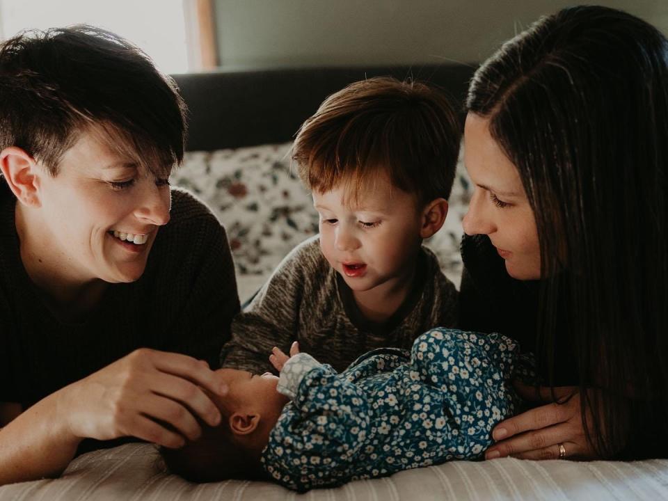 Jackie Kent and her wife Megan pose on a bed with their toddler son and infant daughter.