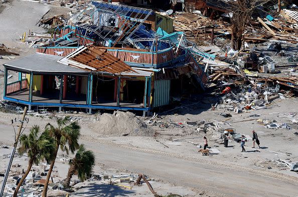 FORT MYERS BEACH, FLORIDA - SEPTEMBER 29: People walk past a building destroyed as Hurricane Ian passed through the area on September 29, 2022 in Fort Myers Beach, Florida. The hurricane brought high winds, storm surge and rain to the area causing severe damage. (Photo by Joe Raedle/Getty Images)