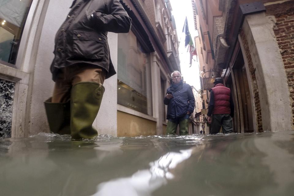 People wade their way through water in Venice, Italy, Friday, Nov. 15, 2019. Exceptionally high tidal waters returned to Venice on Friday, prompting the mayor to close the iconic St. Mark's Square and call for donations to repair the Italian lagoon city just three days after it experienced its worst flooding in 50 years. (AP Photo/Luca Bruno)