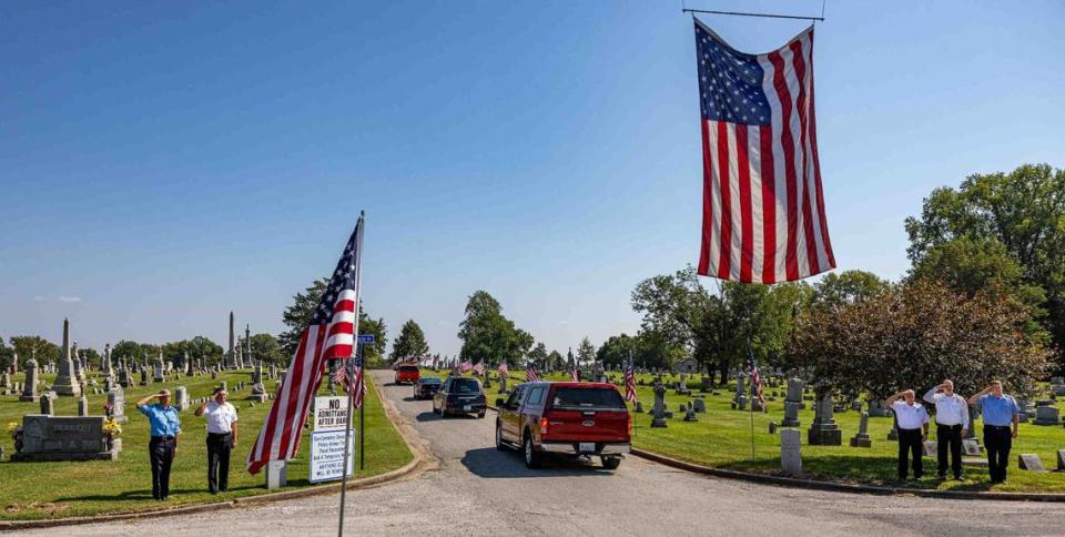 Firefighters salute as the funeral procession for U.S. Marine Capt. Eleanor “Ellie” Cooke, formerly LeBeau, goes under a giant American flag at Mt. Carmel Catholic Cemetery in Belleville on Saturday.