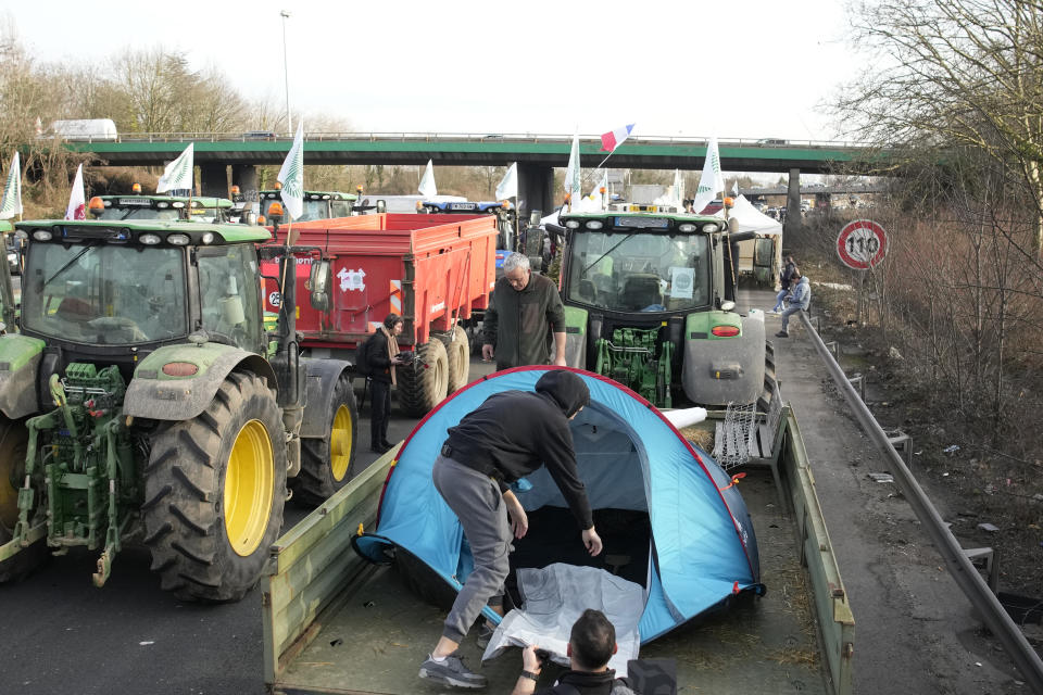 A farmer sets up his tent on the trailer of his tractor on a highway, Monday, Jan. 29, 2024 in Argenteuil, north of Paris. Protesting farmers were encircling Paris with tractor barricades and drive-slows on Monday, using their lumbering vehicles to block highways leading to France's capital to pressure the government over the future of their industry, which has been shaken by repercussions of the Ukraine war. (AP Photo/Christophe Ena)