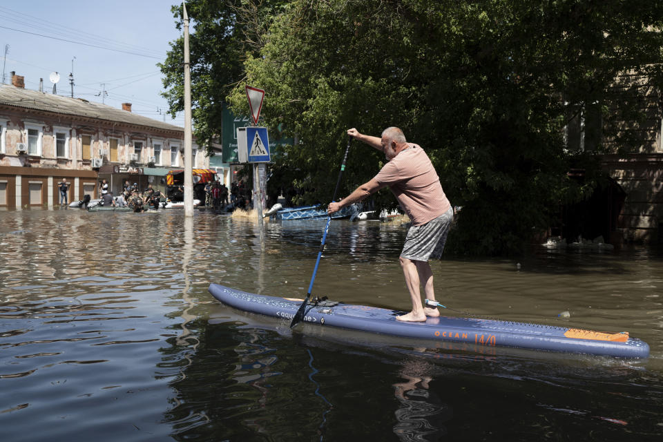 A man uses a stand up paddle board to reach his house in a flooded neighborhood in Kherson, Ukraine, Wednesday, June 7, 2023 after the Kakhovka dam was blown up. Residents of southern Ukraine braced for a second day of swelling floodwaters on Wednesday as authorities warned that a Dnieper River dam breach would continue to unleash pent-up waters from a giant reservoir. (AP Photo/Roman Hrytsyna)