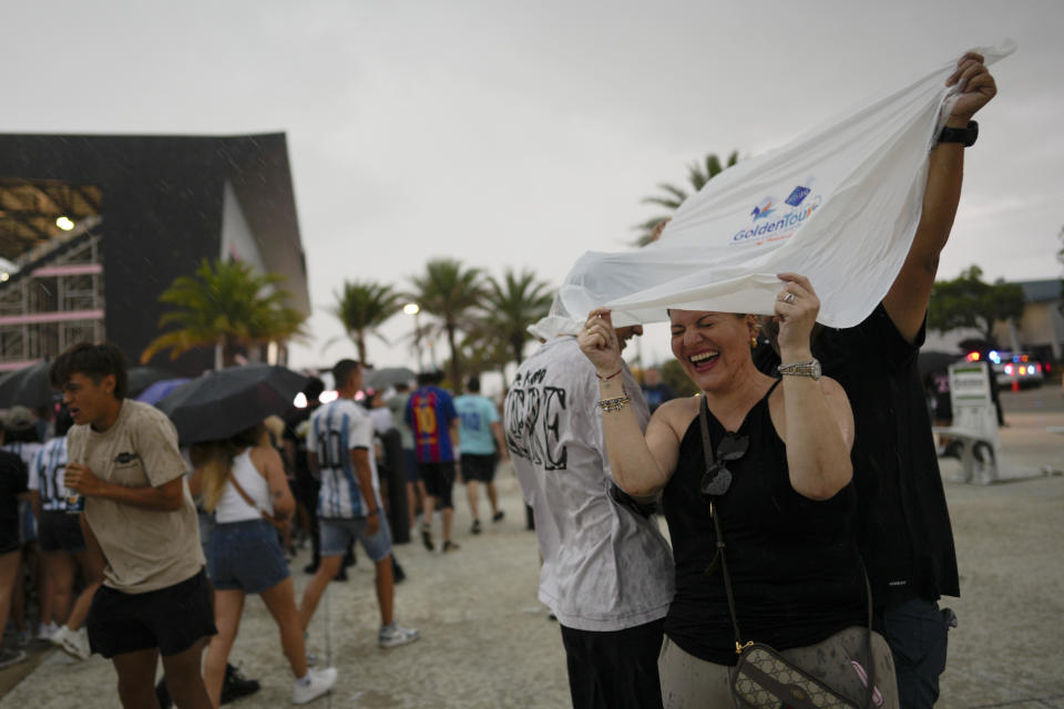 Fans seek shelter from the rain as they wait to enter DRV Pink Stadium, home of the Inter Miami MLS soccer team, for an event to present international superstar Lionel Messi one day after the team finalized his signing through the 2025 season, Sunday, July 16, 2023, in Fort Lauderdale, Fla. (AP Photo/Rebecca Blackwell)