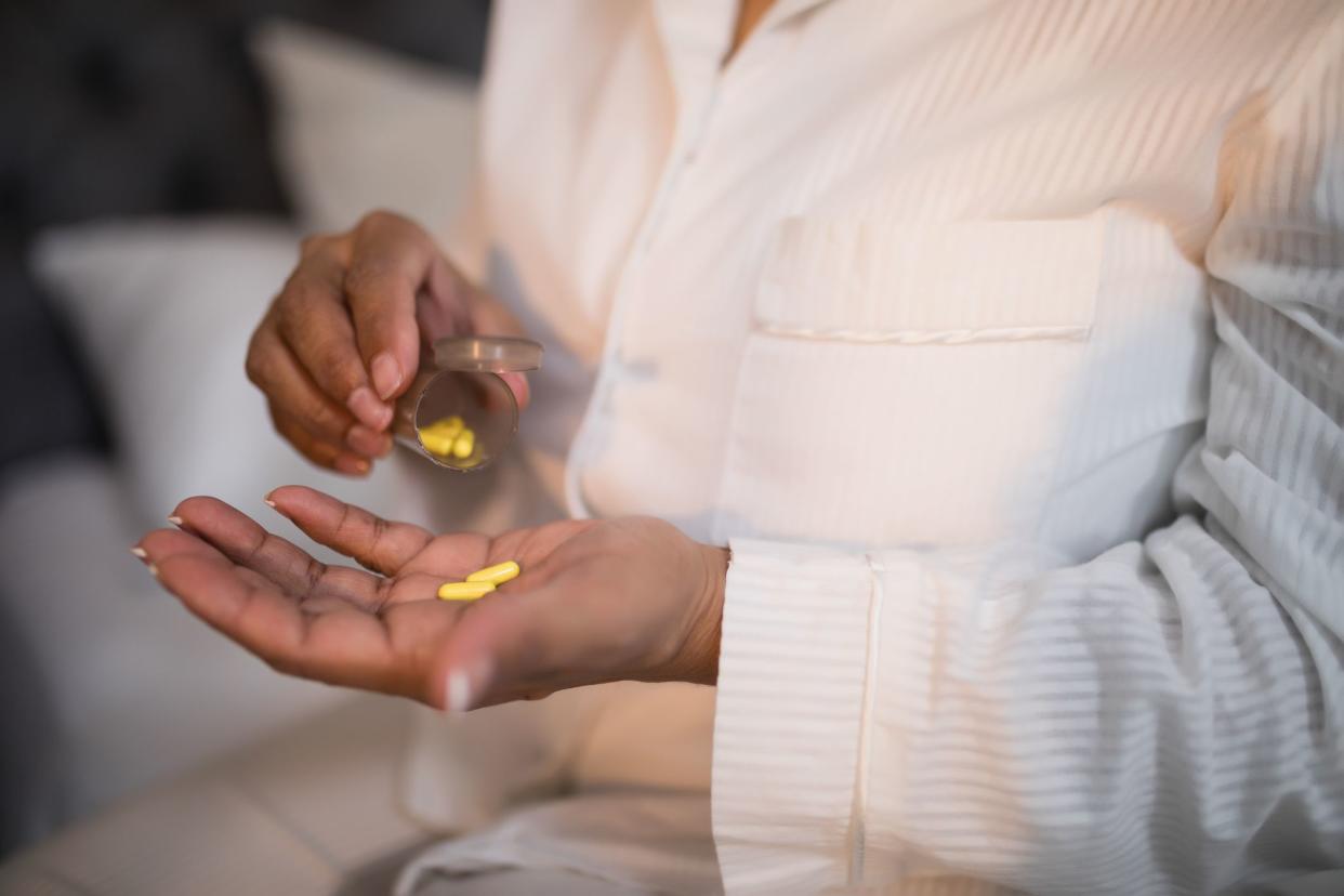 Mid section of woman taking pills in bedroom