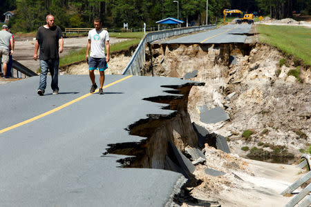 Local residents walk along the edge of a collapsed road that ran atop Patricia Lake's dam after it collapsed in the aftermath of Hurricane Florence, in Boiling Spring Lakes, North Carolina, U.S., September 19, 2018. REUTERS/Jonathan Drake