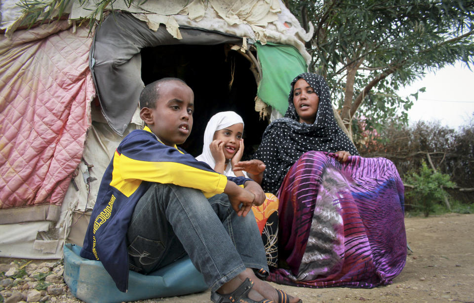 In this photo taken Sunday, April 27, 2014, Ubah Mohammed Abdule, 33, right, sits with her son Abdullahi Yusuf Ahmed, 8, left, and daughter Neshad Yusuf Ahmed, 5, center, outside her hut in the Shedder refugee camp near the town of Jigjiga, in far eastern Ethiopia. The Somali mother’s home is a small shelter with a frame of sticks covered by ragged blankets on the dusty grounds of a refugee camp but it was to her that her 15-year-old son Yahya Abdi wanted to travel to on an impossible journey as a stowaway on a plane from California. (AP Photo/Elias Asmare)
