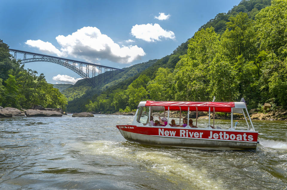 FILE - The Miss M. Rocks idles in the outflow of the New River's Old Nasty rapids, with the New River Gorge Bridge in the background, July, 20, 2022, near Fayetteville, W.Va. A program offering cash and free outdoor adventures to remote workers to move to West Virginia with the hope of offsetting population losses has added the New River Gorge region where out-of-state workers can apply to live. The public-private program Ascend West Virginia said Tuesday, June 20, 2023, that applications are being accepted for the scenic region. (Kenny Kemp/Charleston Gazette-Mail via AP, File)