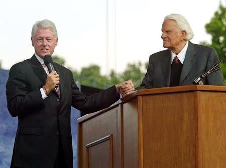 Former United States president Bill Clinton (L) clasps hands with evangelist Billy Graham during the second day of Graham's Crusade at Flushing Meadows Park in New York June 25, 2005. REUTERS/Shannon Stapleton/File Photo