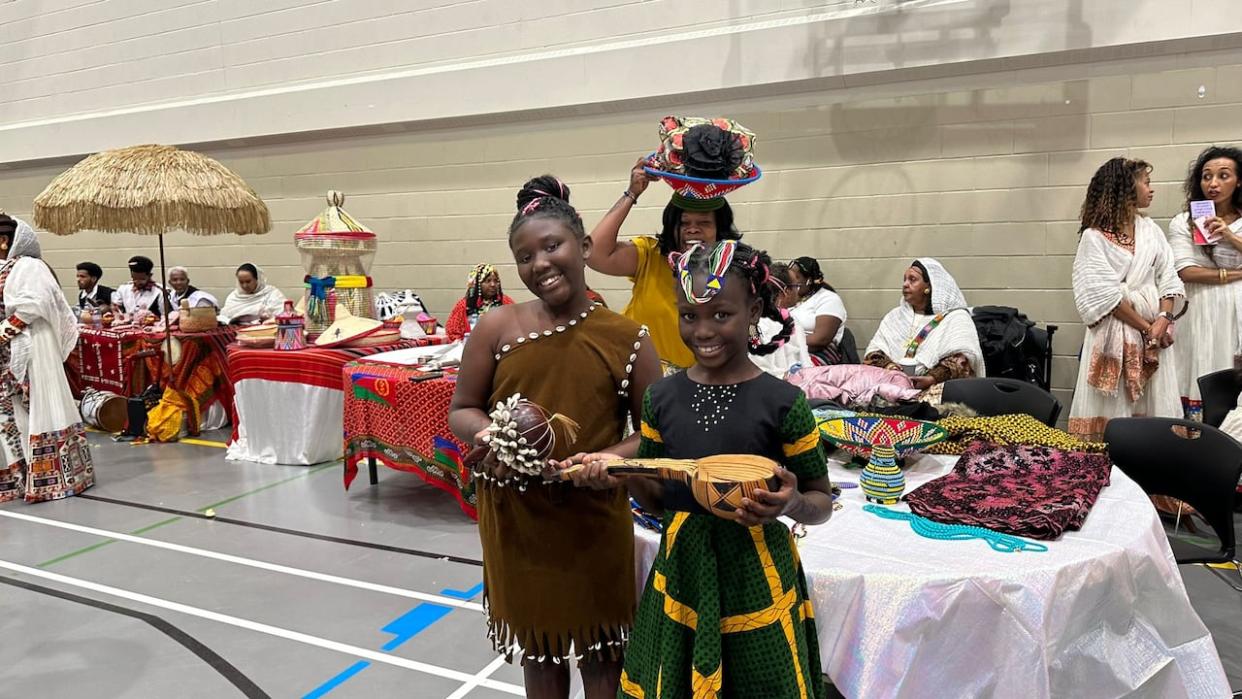 Blessing Jal, left, holds an instrument played when babies are crying in South Sudanese culture. Beside her, Ruth Jal holds a drinking cup called an Adungk. Behind them, Nemisa Simon balances a bread tray on her head as the three of them celebrate their culture and share stories with CBC Calgary on Saturday.  (Akeir Kuol - image credit)