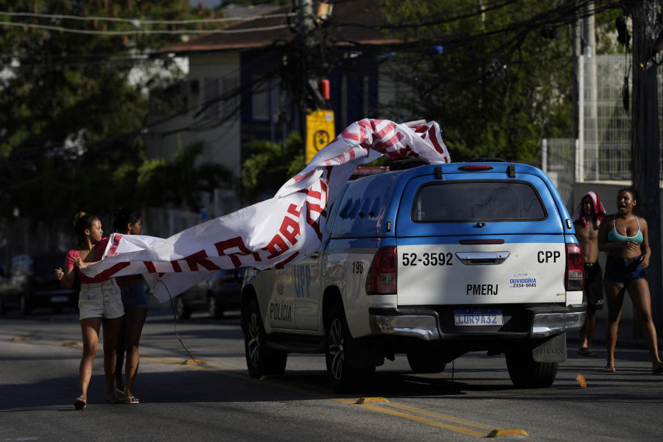 Police drive through a banner with a message that reads in Portuguese: "Out from the favela killer police", that was being held by residents in protest against a police operation that resulted in multiple deaths, in the Complexo do Alemao favela in Rio de Janeiro, Brazil, Thursday, July 21, 2022. Police said in a statement it was targeting a criminal group in Rio largest complex of favelas, or low-income communities, that stole vehicles, cargo and banks, as well as invaded nearby neighborhoods. (AP Photo/Silvia Izquierdo)