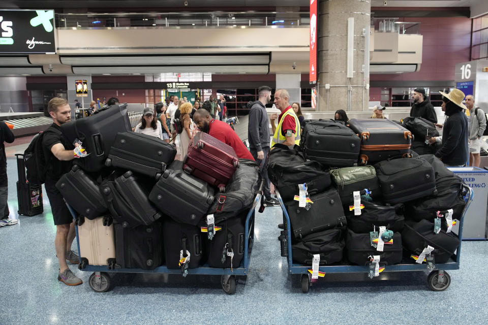Airport baggage handlers and New York Liberty WNBA basketball team staff help stack bags at Harry Reid International Airport, Wednesday, June 28, 2023, in Las Vegas. (AP Photo/John Locher)