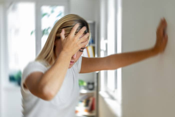 La persona ha le vertigini con la mano sulla fronte e la mano appoggiata al muro per sostenersi