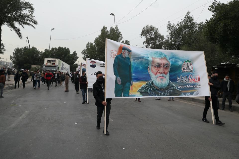 Supporters and members of the Popular Mobilization Forces hold posters of a powerful Iranian general and a top Iraqi militia leader in Baghdad, Iraq, Saturday, Jan. 1, 2022. Hundreds rally in Baghdad on Soleimani assassination anniversary, chanting anti-American slogans, hundreds of people rallied in in the Iraqi capital on the first day of the year Saturday to mark the anniversary of the killing of a powerful Iranian general and a top Iraqi militia leader in a U.S. drone strike. (AP Photo/Khalid Mohammed)