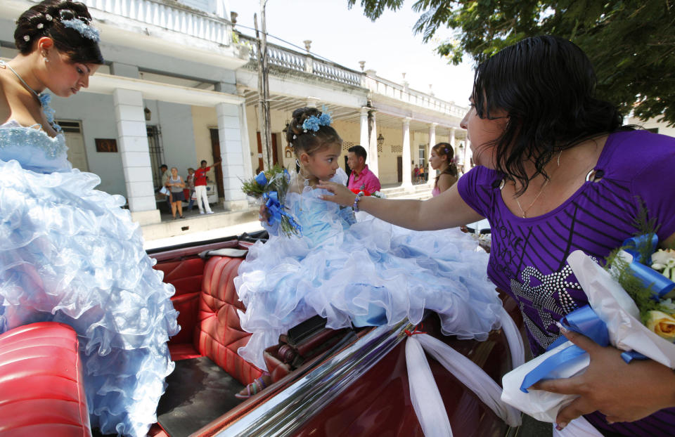 In this Friday April 20, 2012 a mother adjusts her younger daughter's necklace as the girl's sister steps into a rented 1950's era Chevrolet for a parade celebrating the older daughter's quinceanera, a girl's 15th birthday celebration, in Bayamo, Cuba. (AP Photo/Kathy Willens)