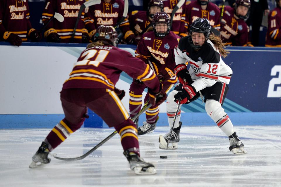 Ohio State's Jennifer Gardiner (12) advances the puck past Minnesota-Duluth's Taylor Stewart (21) during the first period of the NCAA Frozen Four championship hockey game, Sunday, March 20, 2022, in State College, Pa. (AP Photo/Gary M. Baranec)