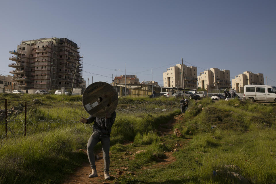 A Palestinian man carries an empty spool from the construction site where he works on a new building in the West Bank Jewish settlement of Efrat, Tuesday, March 16, 2021. Israel went on an aggressive settlement spree during the Trump era, according to an AP investigation, pushing deeper into the occupied West Bank than ever before and putting the Biden administration into a bind as it seeks to revive Mideast peace efforts. (AP Photo/Maya Alleruzzo)