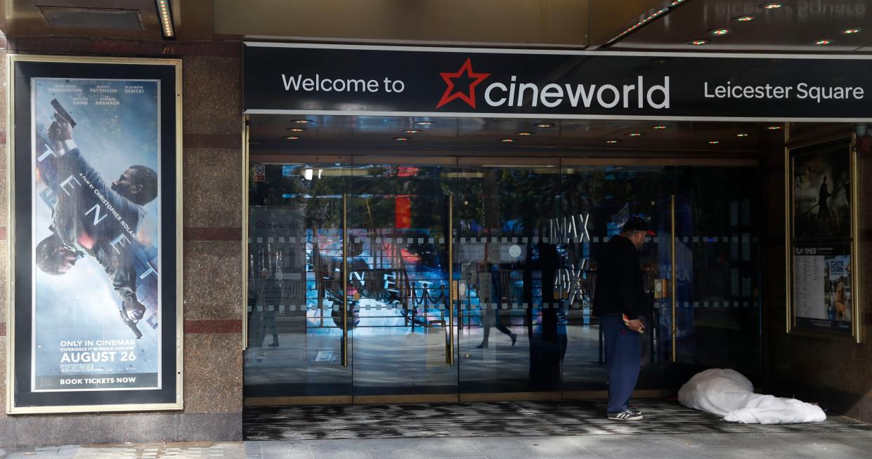 A man talks to a person sleeping in the doorway of a Cineworld cinema in Leicester Square, London on Monday, Oct. 5, 2020. The company Cineworld have confirmed that all the 127 UK Cineworld cinemas will temporarily close, affecting some 5,500 employees, due to the ongoing coronavirus pandemic and the lack of movies at are being released.