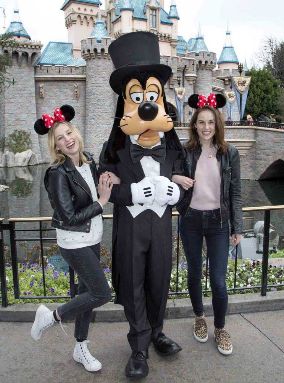 <p><em>Downton Abbey</em> stars Laura Carmichael and Michelle Dockery donned their Minnie Mouse ears for a portrait with a very dapper Goofy during their visit to Sleeping Beauty's castle in February.</p>