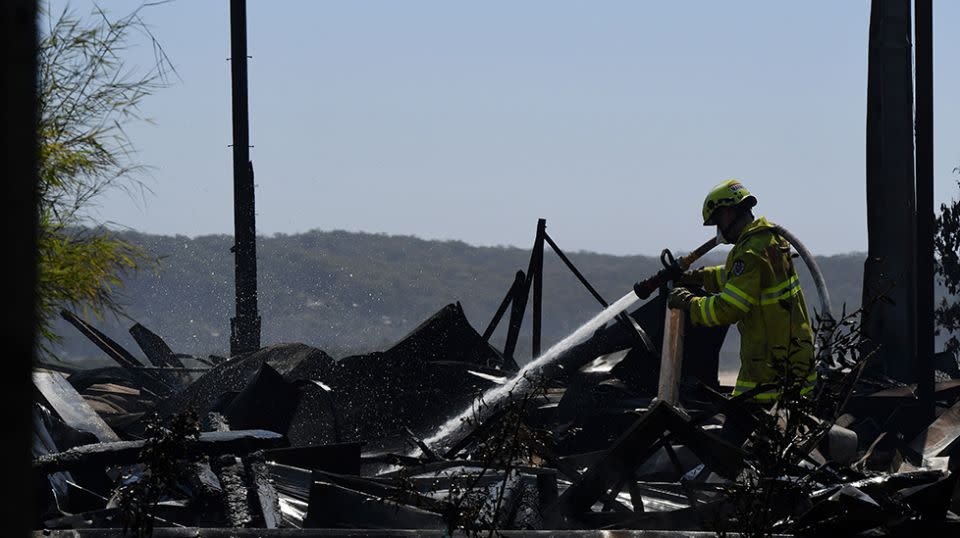 A firefighter extinguishes the charred embers of a home destroyed in the bushfire. Source: AAP