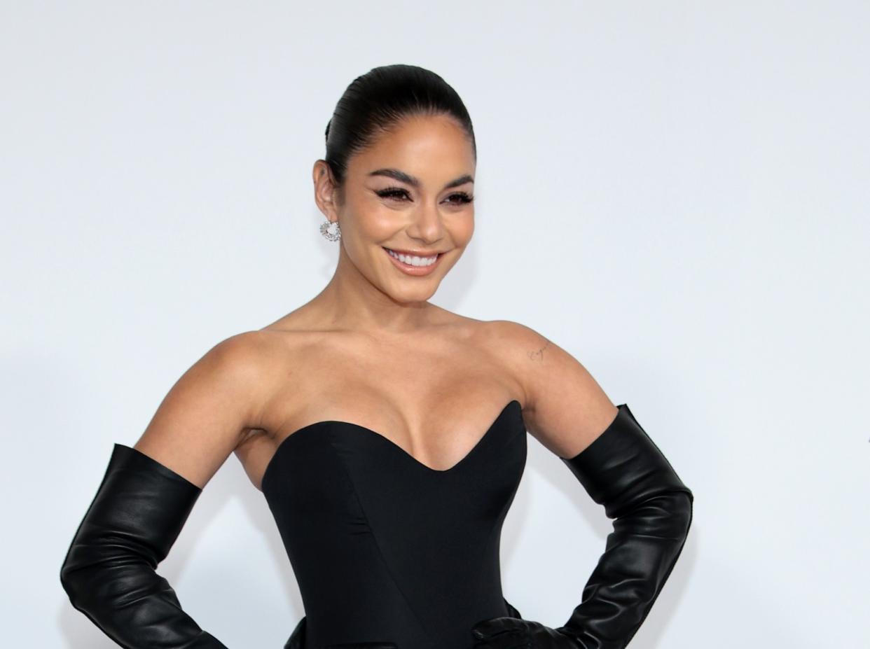  A headshot of Vanessa Hudgens smiling in a black strapless dress . 