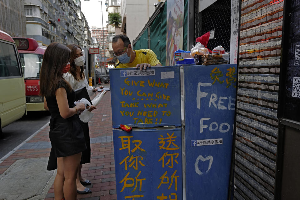 Two women chat with Ahmed Khan, center, yellow shirt, after putting foods inside a refrigerator at Woosung Street in Hong Kong's old-school neighborhood of Jordan Wednesday, Nov. 18, 2020. Khan, founder of a sports foundation on the same street, said he was inspired to create a community refrigerator after seeing a film about others doing the same thing. He found the refrigerator at a nearby refuse collection point and painted it blue. (AP Photo/Vincent Yu)