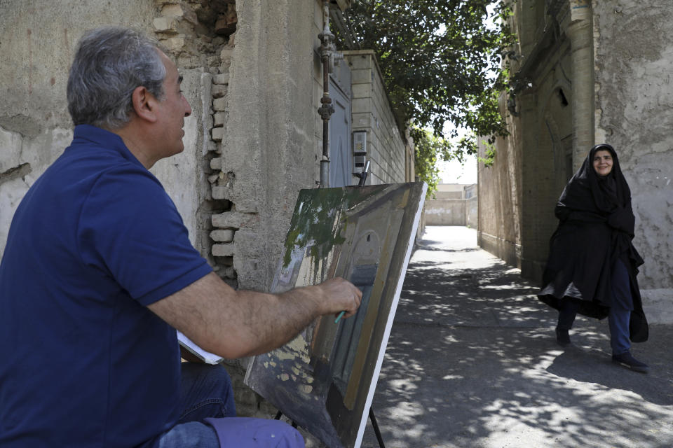 El pintor Hassan Naderali saluda a una residente mientras pinta un edificio antiguo en el barrio histórico de Oudlajan, en Teherán, Irán, el lunes 20 de junio de 2022. (Foto AP/Vahid Salemi)