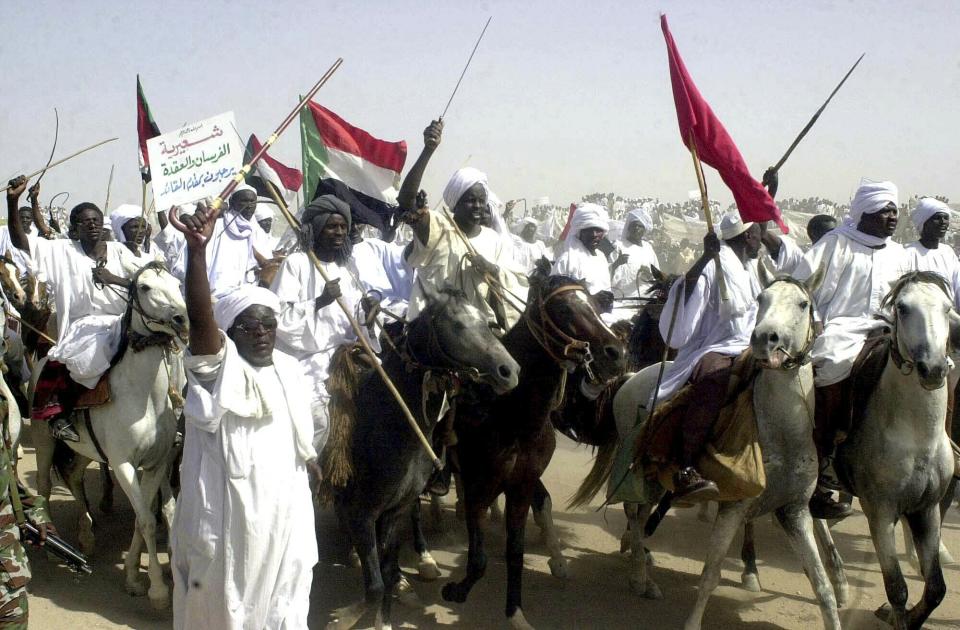 FILE - In this May 19, 2004 file photo, Arab and African horsemen from Sudan's Shairia locality parade before then Sudanese President Omar Al-Bashir, as a show of solidarity in Nyala, capital of the country's southern Darfur state. al-Bashir, driven from power and now languishing in a prison where his opponents were once jailed and tortured, is more vulnerable than ever to a decade-old international arrest warrant for war crimes committed in Darfur. But the military, which forced him from power after four months of mass protests, has said it will not extradite him to the International Criminal Court at the Hague. (AP Photo/Abd Raouf, File)