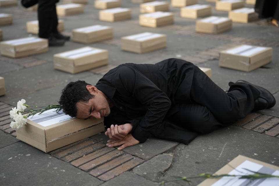 A man lies among boxes representing symbolic coffins as he remember former guerrillas and social leaders who have been killed since the 2016 signing of a peace agreement between rebels of the Revolutionary Armed Forces of Colombia, FARC, and the government, in Bogota, Colombia, Tuesday, Feb. 20, 2024. (AP Photo/Fernando Vergara)