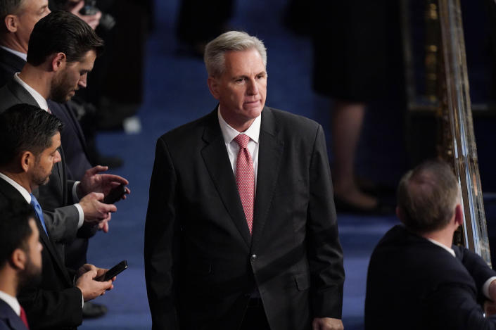 Kevin McCarthy stands near others who are looking into their cellphones.
