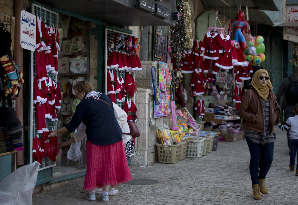 In this Thursday, Dec. 5, 2019, photo, Christian visitors shop near the Church of the Nativity, traditionally believed by Christians to be the birthplace of Jesus Christ, in the West Bank city of Bethlehem. As visitors descend on Bethlehem this Christmas, they have the option of staying in restored centuries-old guesthouses, taking food tours of local markets, and perusing the dystopian art in and around a hotel designed by the British graffiti artist Banksy.(AP Photo/Majdi Mohammed)
