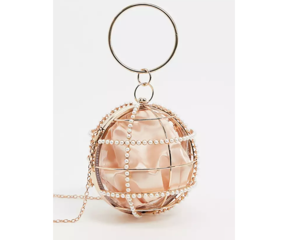 A gold and pearl studded cage circular clutch bag with peach silk interior and a gold circle handle on the top against a pale grey background.
