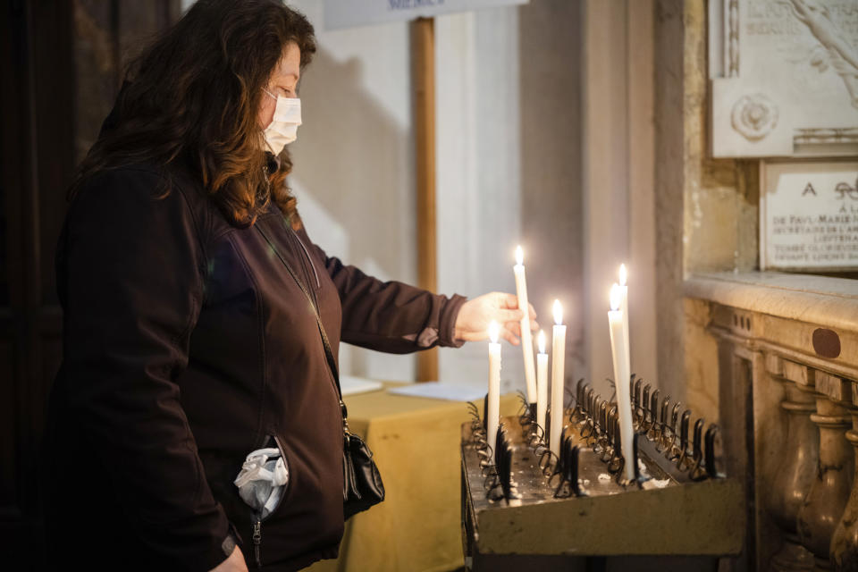 Una mujer con mascarilla enciende una vela en la iglesia de San Luis de los Franceses en Roma, el miércoles 4 de marzo de 2020. La iglesia es muy conocida por albergar en una de sus capillas un conjunto de pinturas de Caravaggio. (AP Foto/Domenico Stinellis)