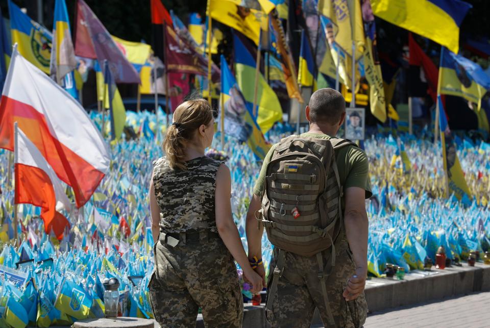 A couple in uniform hold hands as they pass Ukrainian national flags set up commemorating fallen Ukrainian soldiers (EPA)