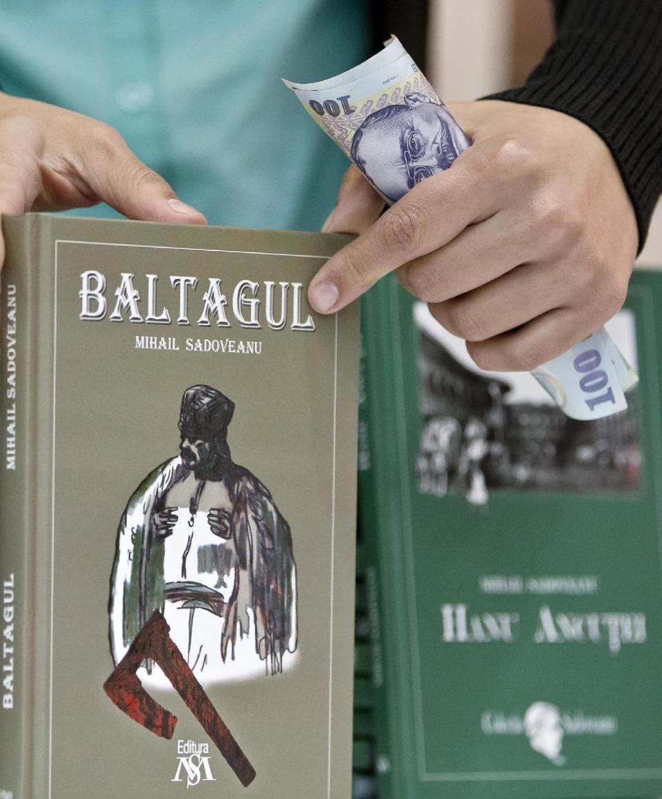 In a Nov. 14, 2013, photo, a woman holds money while selling republished novels by Romanian writer Mihail Sadoveanu in Bucharest, Romania. He is one of Romania’s greatest writers, but his work couldn’t be found in bookstores. Now, they are finally getting their place back on the shelf. (AP Photo/Vadim Ghirda)