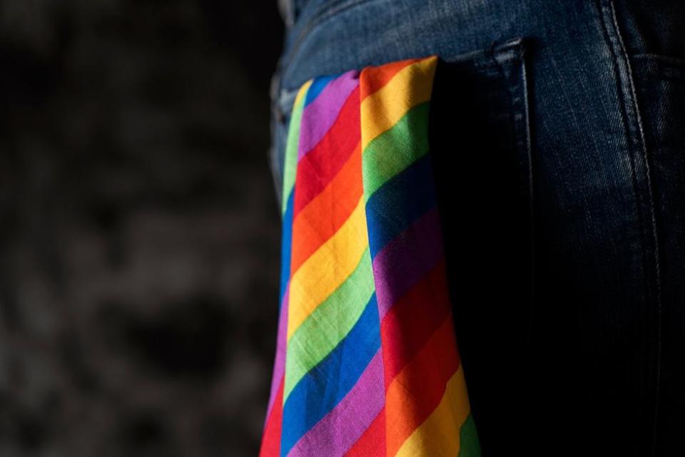 closeup of a young caucasian person with a rainbow-patterned handkerchief hanging from the back pocket of his or her jeans, againsta a dark background with some blank space