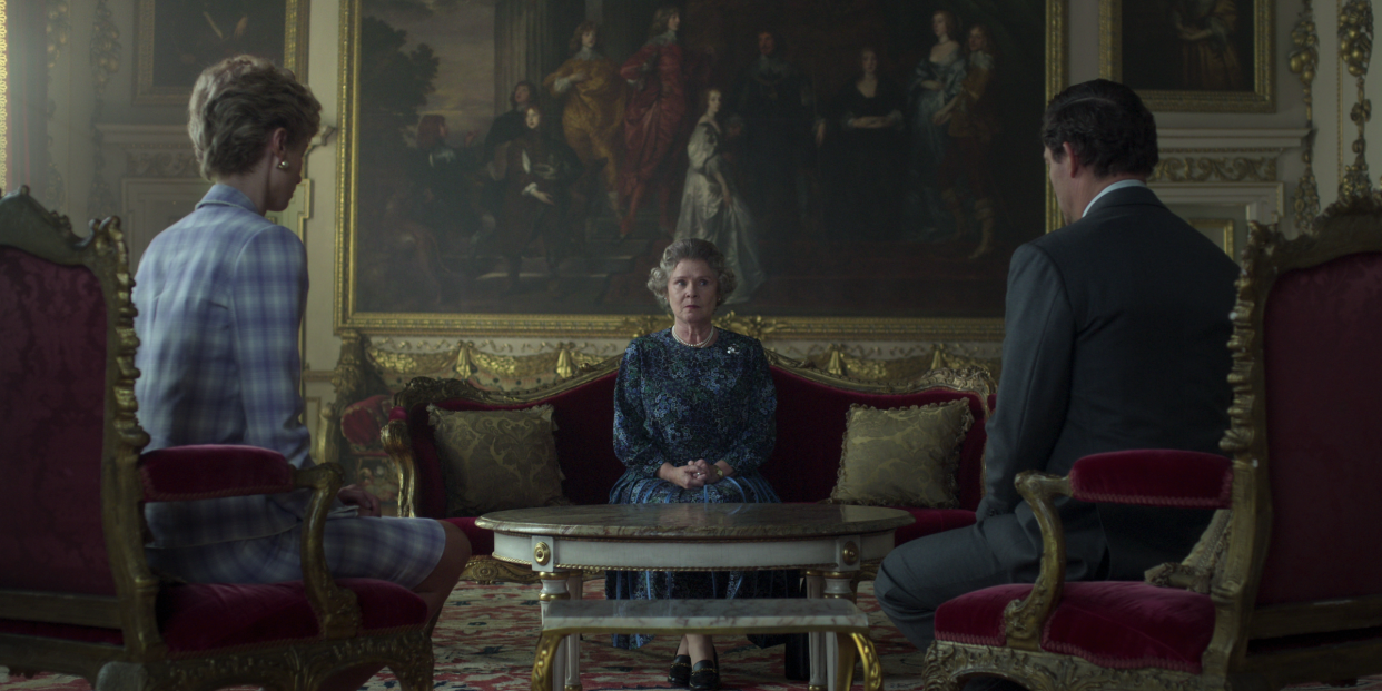 Queen Elizabeth II sits on a red velvet couch with an advisor on either side.