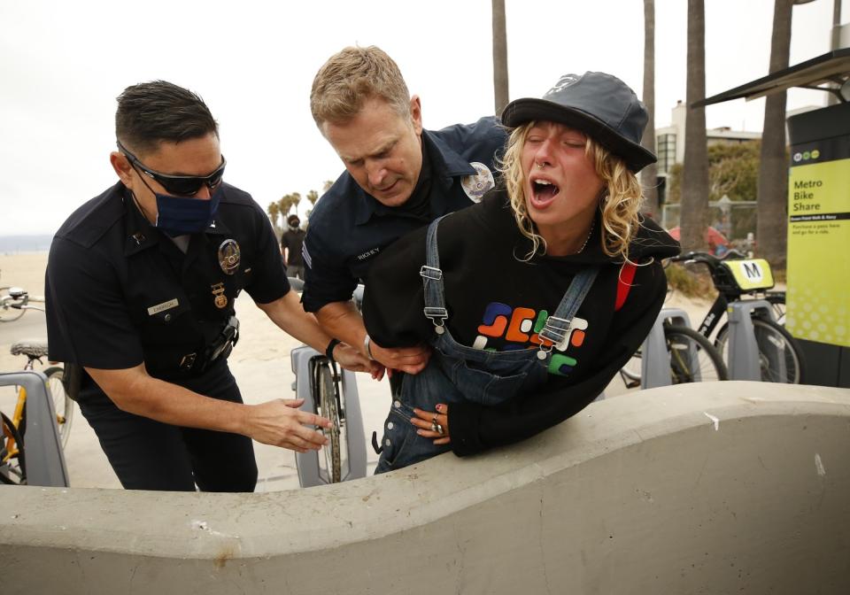 A woman yells as police put her hands behind her back next to a concrete bench at the beach.
